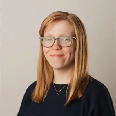 Portrait of Crystal Carter smiling, with shoulder-length strawberry blonde hair and glasses